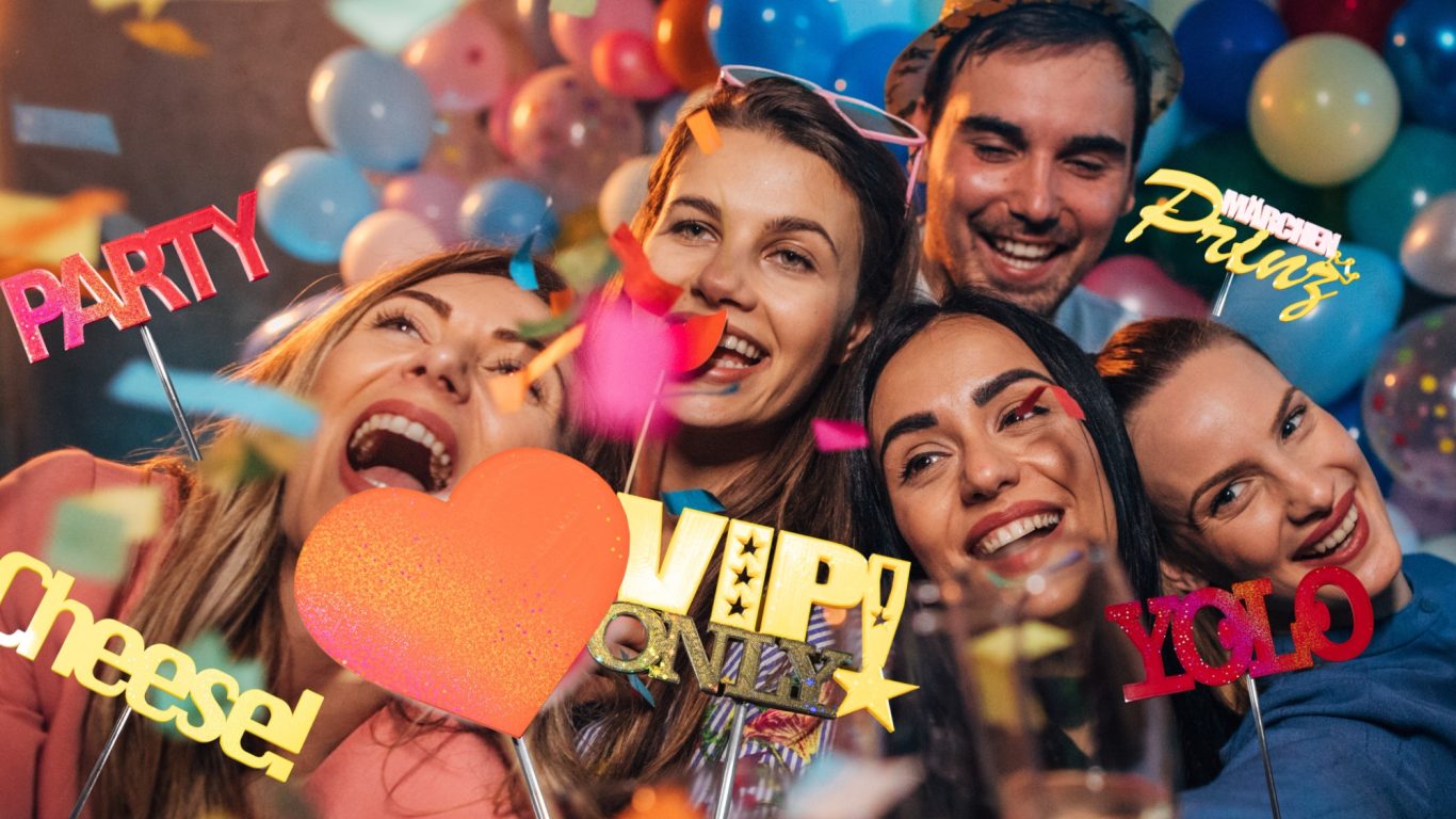 Fröhliche Gruppe junger Menschen mit Luftballons und Konfetti, feiern und lachen.