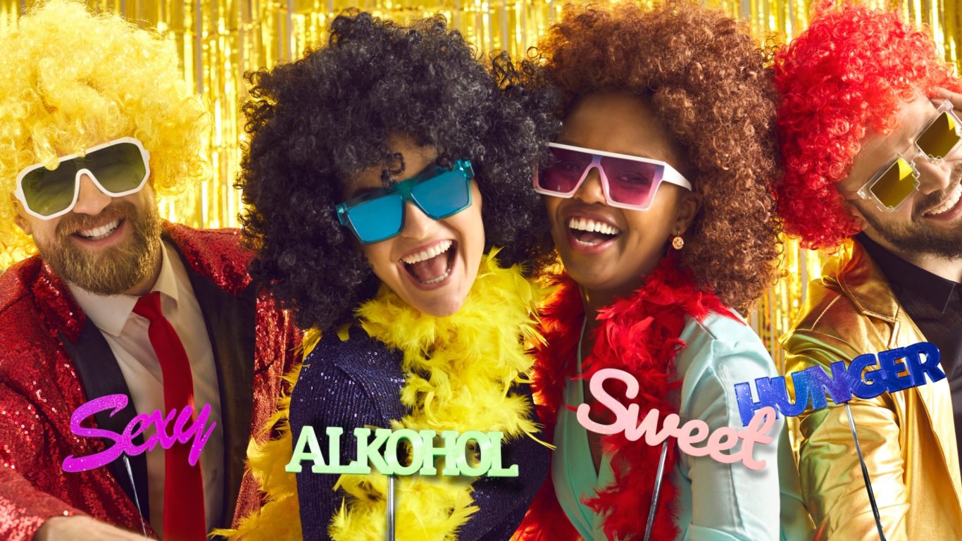 Viere farbenfrohe Personen in witzigen Kostümen feiern mit Sonnenbrillen und Pailletten.